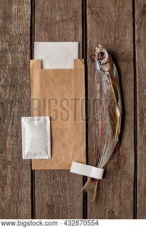 Air-dried Sabrefish With Kraft Paper Bag, Wet Wipe And Paper Napkin On Wooden Surface