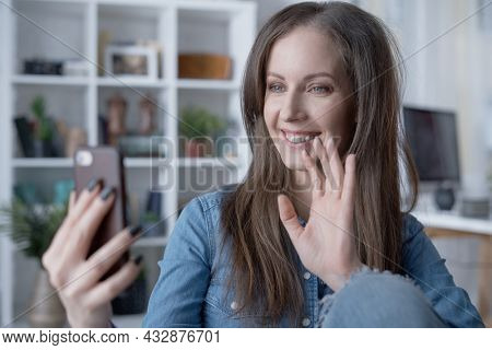 Happy white woman talking on video chat with phone at home. Conference call with friend, family or work. Video blogger working, sitting in living room, taking selfie.
