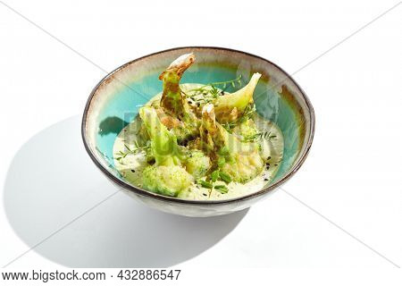 Fried tempura broccoli with peanut sauce in bowl. Vegeterian hot dish - florets cabbages roasted  in klar on white background. Veggie menu for asian restaurant. Hot vegan appetizers plant based