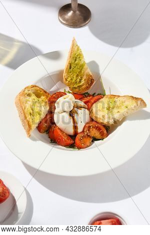 Traditional Italian salad with Burrata cheese and tomatoes. Fancy caprese with burrata cheese, cherry tomatoes, pesto and balsamic sauces. Summer dish with mozzarella cheese on white table with shadow