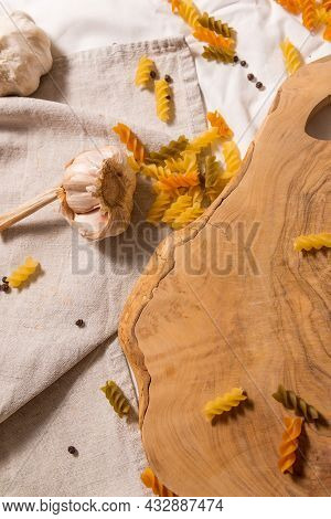 Fragment Of Cutting Board Curved Shape Of Olive Tree, Scattered Around Pasta, Garlic, Pepper. They L
