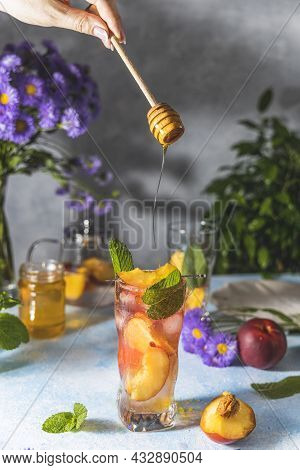 Woman Hand Perfused Honey On Peach Infused Water, Cocktail, Lemonade Or Tea. Summer Iced Cold Drink 