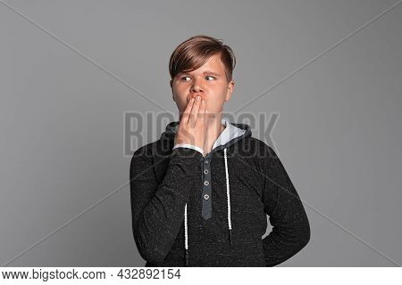 Teen Boy Cover Mouth With Hand Shocked With Shame For Mistake, Stands Over Grey Background, Wearing 