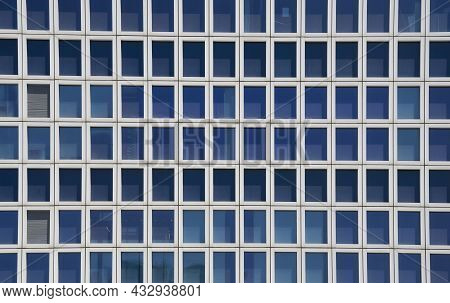 A Segment Of A Typical High Rising Building, With Many Metal Framed Blue Glass Windows And Two Close