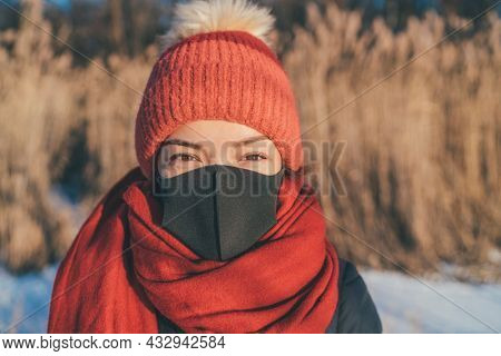 Face mask wearing Asian woman portrait in outdoor winter. Girl in cold weather accessories, hat, scarf for frost bite.