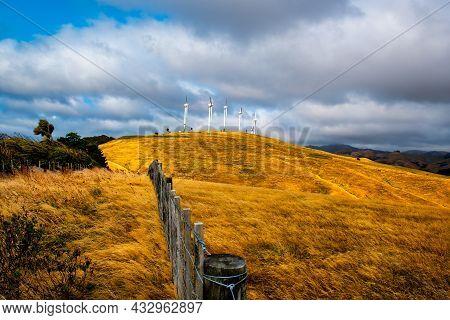 Rural Wooden Post And Wire Farm Fence Leading The Way Over Dry Arid Farmland To A Group Of Wind Turb