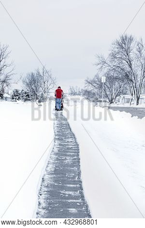 A Man In Red Winter Clothes Cleaning Snow By Using A Snowblower At The Long Walkway In Bright Day An