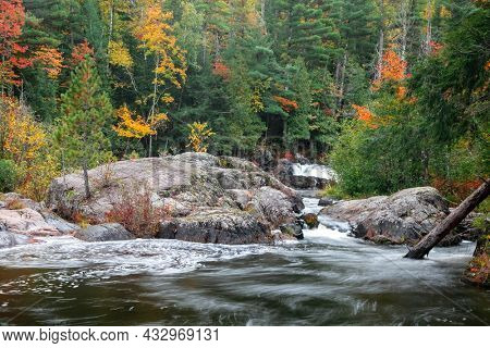 Large rocks in running water of Dead river surrounded with fall foliage in Michigan upper peninsula.
