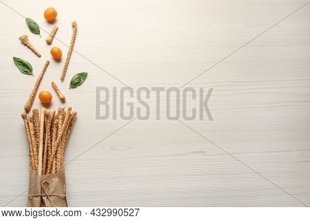 Delicious Grissini Sticks, Basil Leaves And Yellow Tomatoes On White Wooden Table, Flat Lay. Space F