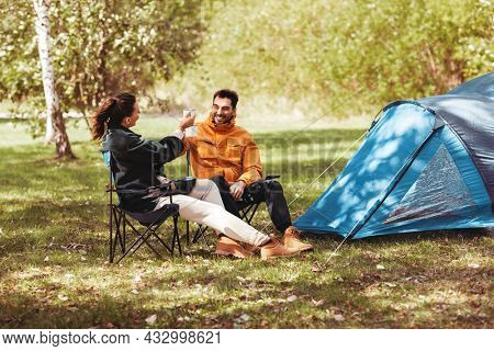 camping, tourism and travel concept - happy couple drinking tea at tent camp