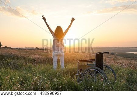 Woman Standing Near Wheelchair In Evening Outdoors, Back View. Healing Miracle