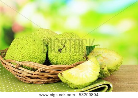 Osage Orange fruits (Maclura pomifera) in basket, on wooden table, on nature background