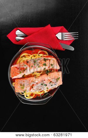 fresh fried natural pink salmon on italian traditional tagliatelle backed with tomato and vegetables served over black wooden table