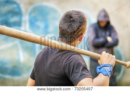 Aggressive teenager with a baseball bat against man at outdoor