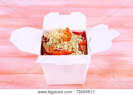 Chinese noodles with meat and pepper in takeaway box on pink background