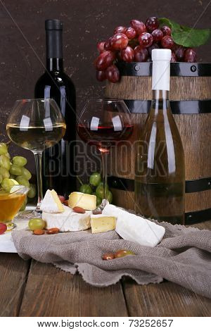 Supper consisting of Camembert and Brie cheese, honey, wine and grapes on sackcloth on stand and wine barrel on wooden table on brown background