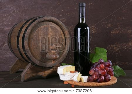 Supper consisting of Camembert cheese, wine and grapes on cutting board and wine barrel on wooden table on brown background