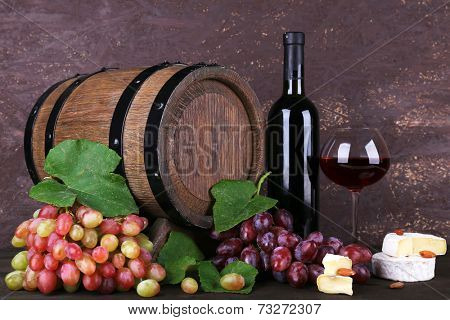 Wine in bottle and in goblet, Camembert and brie cheese, grapes and wooden barrel on wooden table on wooden background