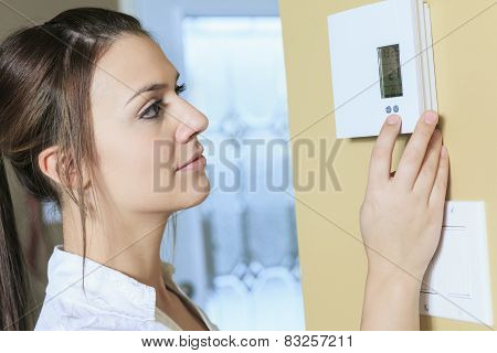 A woman set the thermostat at house.