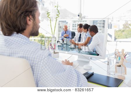 Desinger working on his computer against group of business people brainstorming together