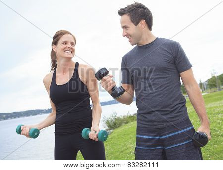A Young, caucasian couple working out with dumbbells outside