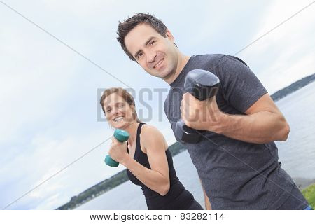 A Young, caucasian couple working out with dumbbells outside