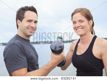 A Young, caucasian couple working out with dumbbells outside