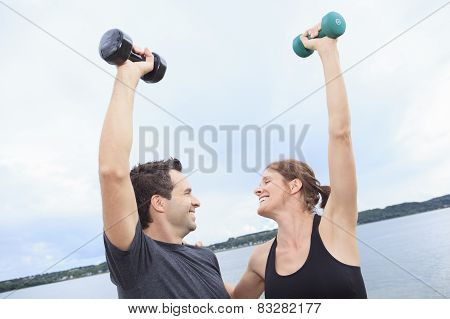 A Young, caucasian couple working out with dumbbells outside