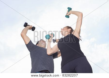 A Young, caucasian couple working out with dumbbells outside