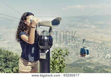 Girl is looking at coin operated binocular on a mountain