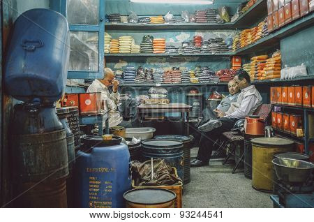 JODHPUR, INDIA - 07 FEBRUARY 2015: Owner of spice store massages forehead after long working day while customers discuss business. Post-processed with added grain and texture.