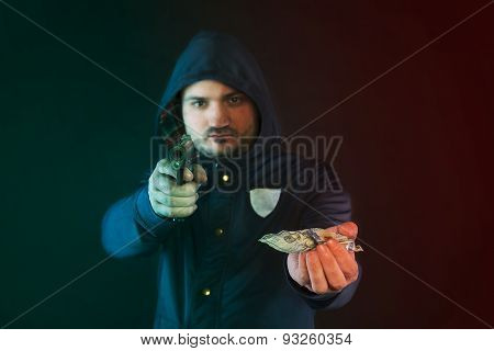 A Person In A Hoodie Is Aiming And Holding The Other Hand With The Dollar Note. A Concept Of The Rob