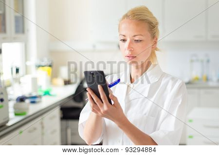Portrait of an attractive, young, confident female health care professional in his working environment making notes on her smarth phone.