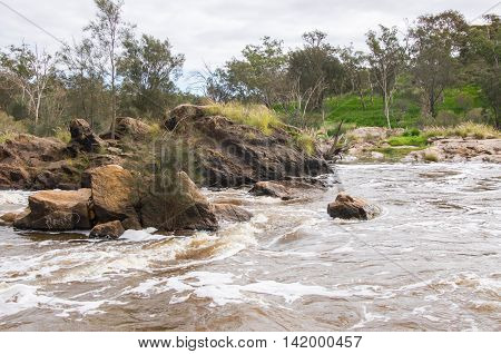 Rocky white waters with lush green landscape at the Bell Rapids under a cloudy sky in the Swan Valley in Western Australia.