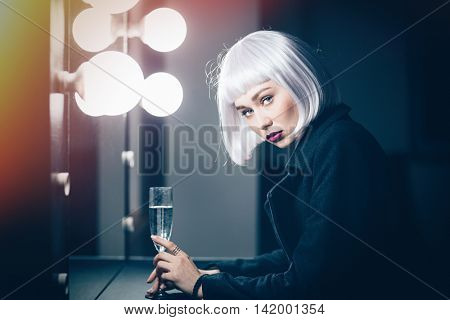 Beautiful serious young woman drinking champaigne near the miror in dressing room