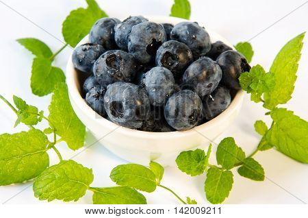 blueberries in a white plate with mint on a white table