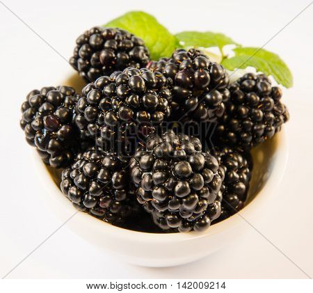 blackberries in a white plate with mint on a white table