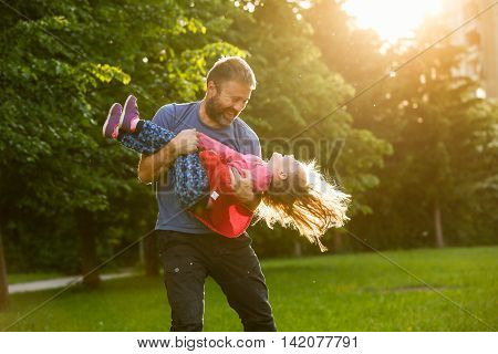 Devoted father spinning his daughter in circles bonding playing having fun in nature on a bright sunny day. Parenthood lifestyle parenting childhood and family life concept.