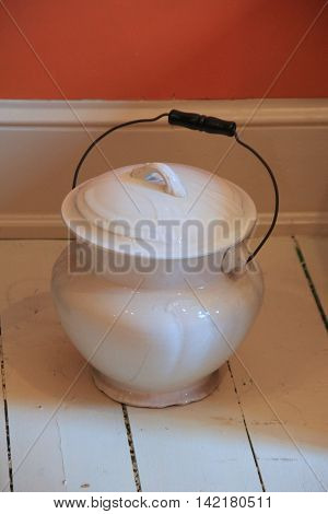 Well-kept white chamber pot with black handle set on white painted wood flooring of room