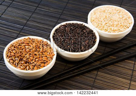 black red and white unpolished rice in white plates on a black straw mat