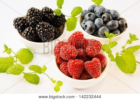 raspberries blackberries blueberries in white plates with mint on a white table