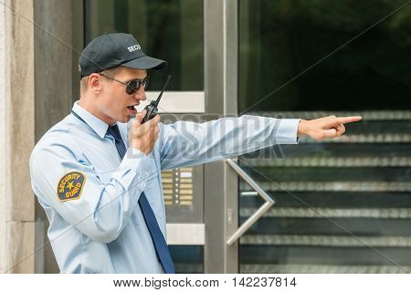 Young Male Security Guard Gesturing While Using Walkie-talkie
