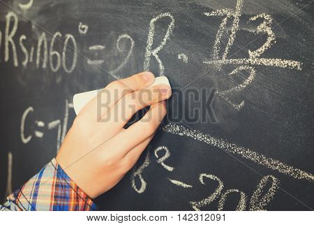 Hand with chalk writting math formulas on black board close up, retro toned