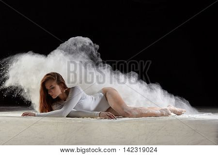 Dance art and dancing in dust. Dancer posing gracefully on the floor in a cloud of dust. Studio portrait of woman dancing with flour.