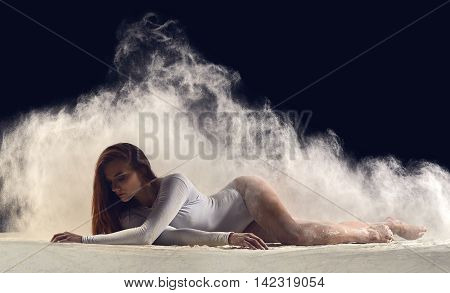 Dancer posing gracefully on the floor in a cloud of dust. Dance art and dancing in dust. Dancer in a white bathing suit.