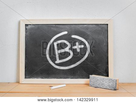 Grade b plus write on dirty blackboard chalk and eraser on wood table over white cement background