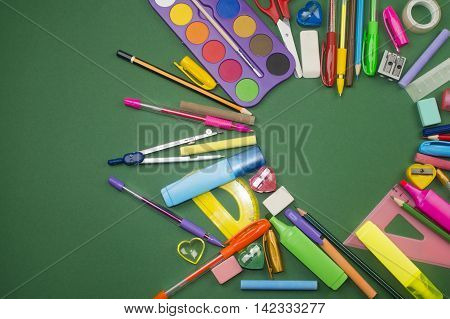 Different school supplies are in heart shape on green background.