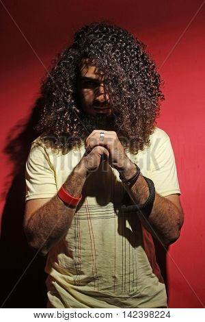 Sexy brunette young guy fashion and long beautiful curly hair against red background looking into the camera