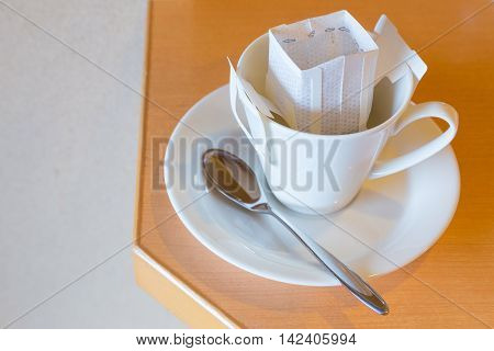 White coffee cup and spoon with white pre-packaged blended coffee in paper filter set