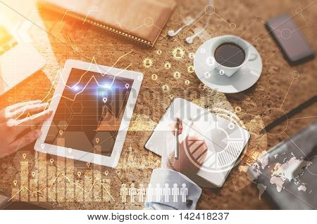 Top view of a man at his workplace in office. Tablet smart phone and coffee on table. Graphs and schemes on foreground. Concept of office work. Toned image. Double exposure